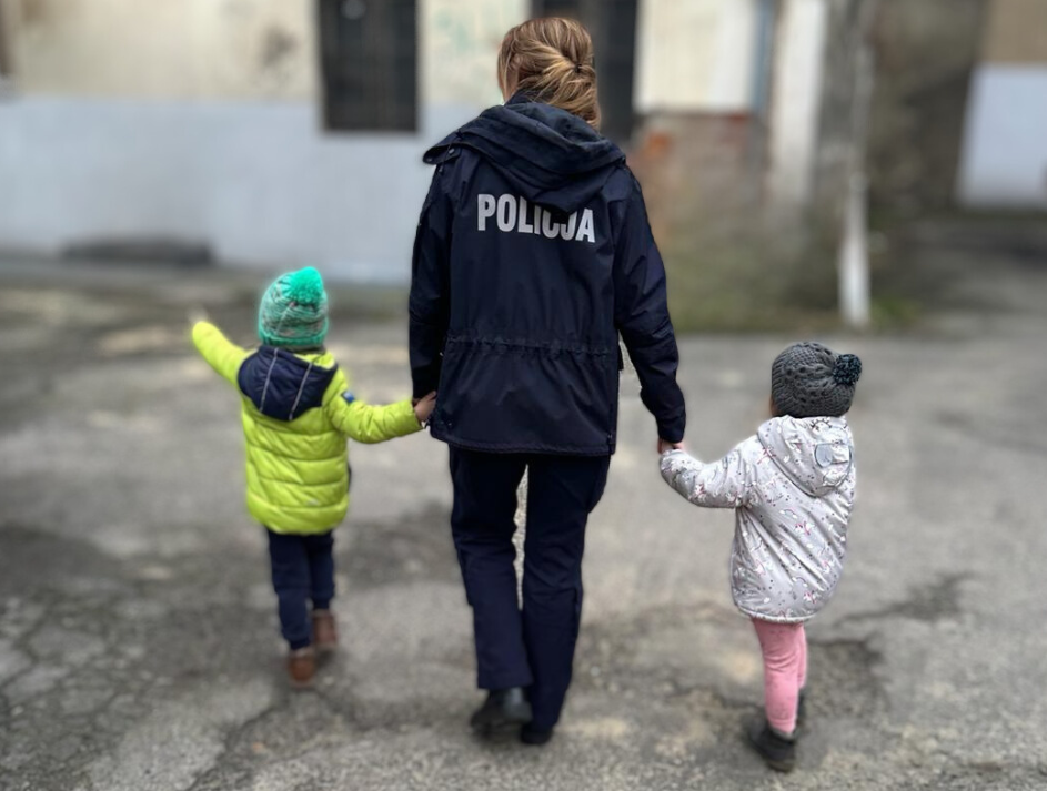 policjantka prowadzi za ręce dwojkę małych dzieci