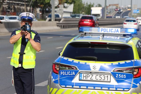 Policjant ruchu drogowego mierzy prędkość nadjeżdżakjących samochodów.