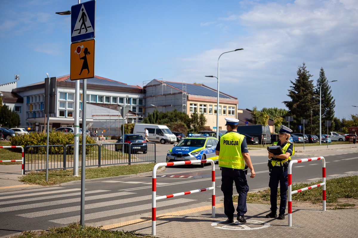 Policjant i policjantka stoją przy przejściu dla pieszych iedaleko szkoły.