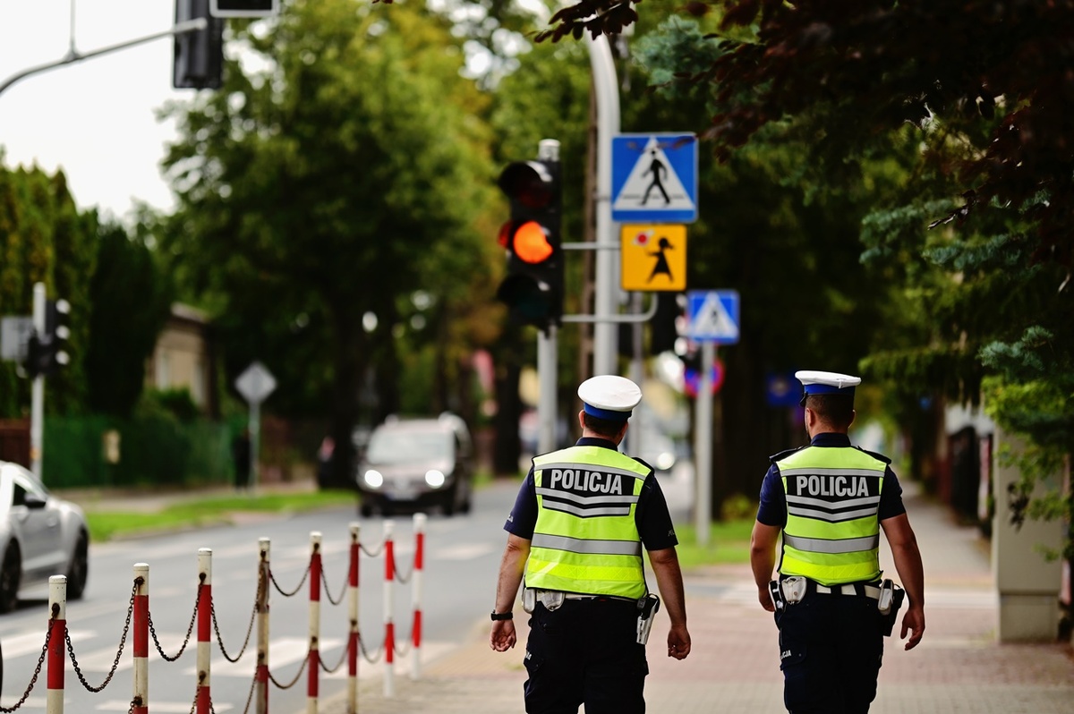Dwaj policjanci idą w kierunku przejścia dla pieszych obok szkoły.