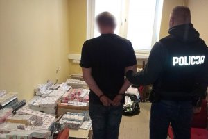 Policjant z zatrzymanym mężczyzną, w tle leżą paczki papierosów