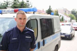 sierżant Piotr Pawelec na tle radiowozu - zdjęcie duże