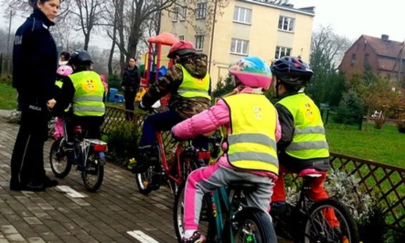 Dzieci na rowerach w towarzystwie policjantki, w kamizelkach odblaskowych