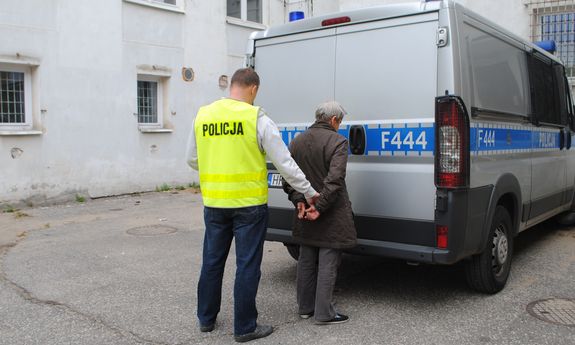 Zatrzymana kobieta i policjant, w tle policyjny radiowóz