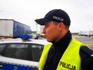 Policjant przy radiowozie, odzyskana naczepa i pojazdy na parkingu