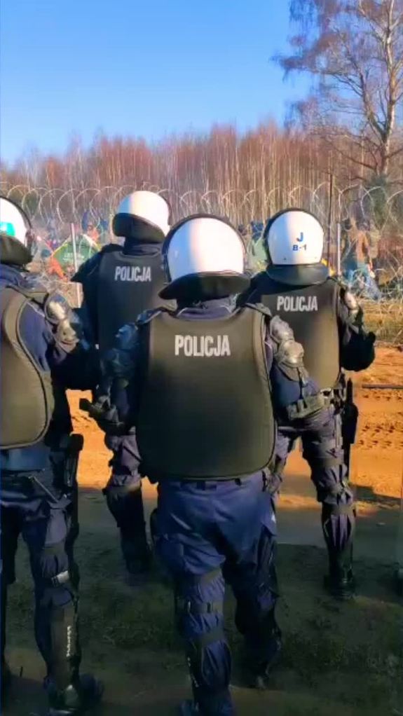 Grupa policjantów w hełmach i kamizelkach widziana od tyłu.