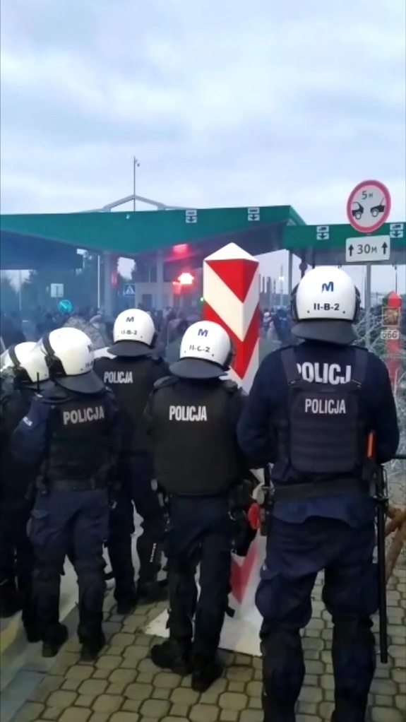 Policjanci w hełmach i kamizelkach przed przejściem granicznym.