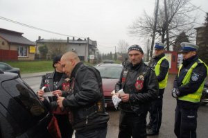 motocykliści naklejający naklejkę na szybę pojazdu w tle policjanci