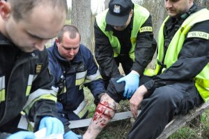 strażacy i policjant udzielający pierwszej pomocy rannemu policjantowi