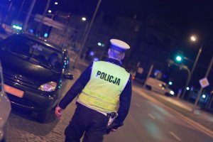 policjant nocą idzie w kierunku zatrzymanego pojazdu