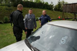 policjanci - na pierwszym planie auto z przestrzelinami w przedniej szybie