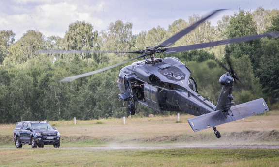 Policyjny Black Hawk widziany od tyłu nisko nad drogą którą nadjeżdża samochód typu SUV.