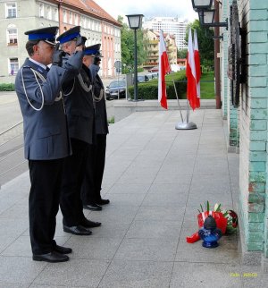 policjanci oddają honory pod tablicą pamiątkową