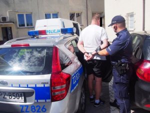 policjant pomaga wsiąść zatrzymanemu do radiowozu