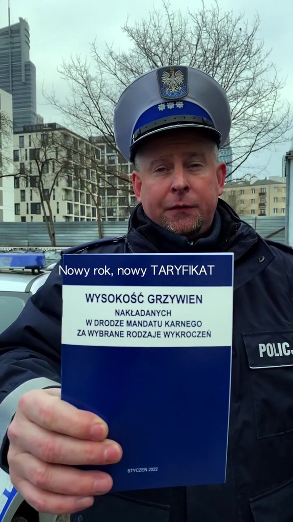 Policjant ruchu drogowego pokazuje taryfikator mandatów.