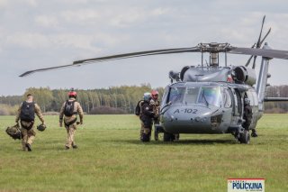 Śmigłowiec na trawiastym lotnisku, w jego kierunku idą trzej funkcjonariusze BOA.