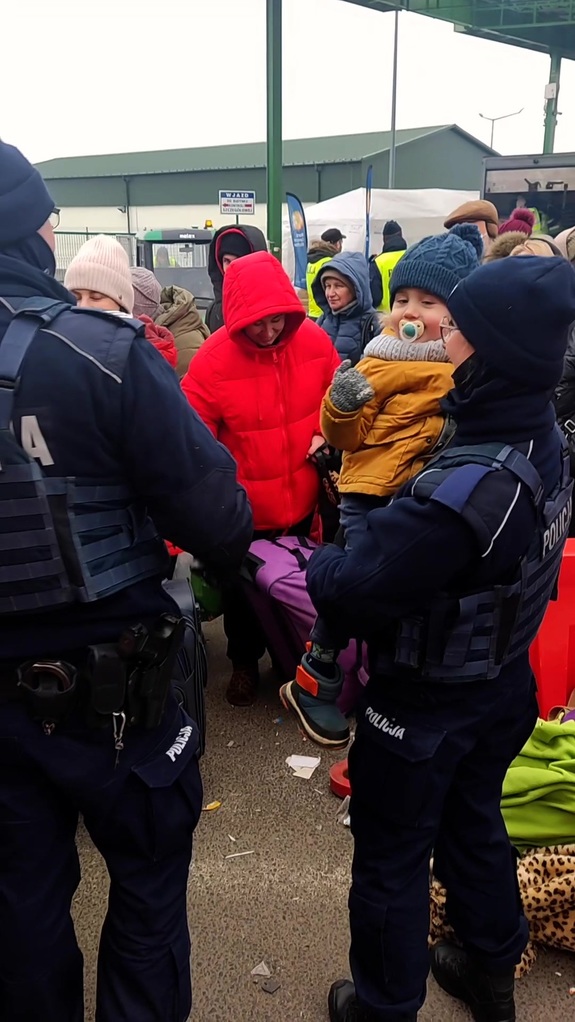Policjantka trzyma na rękach dziecko, obok jej kolega. W tle tłum ludzi.