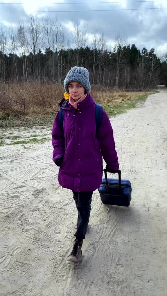 Dziewczynka w ciepłej kurtce i czapce idzie polną drogą ciągnąc walizkę.