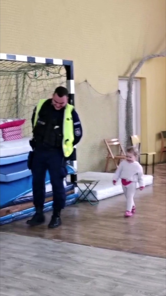 Policjant spaceruje na sali gimnastycznej z małą dziewczynką.