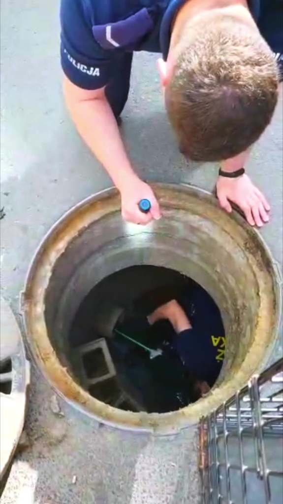 Policjant oświetla latarką wnętrze studzienki kanalizacyjnej.