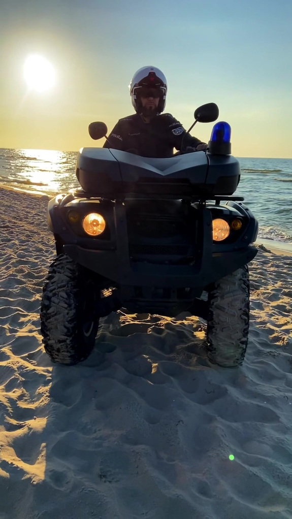 Policjant na quadzie podczas patrolowania plaży, na tle zachodzącego słońca.