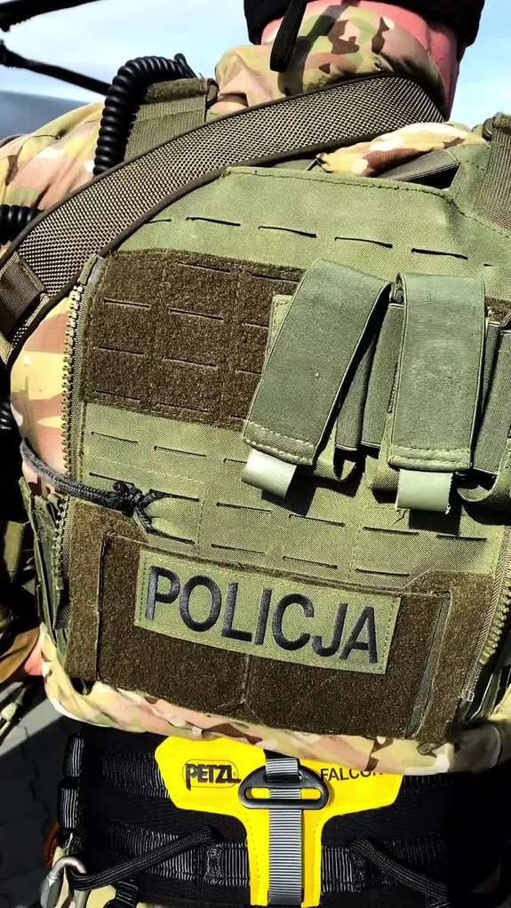 Policjant w kamizelce taktycznej z napisem POLICJA na plecach.