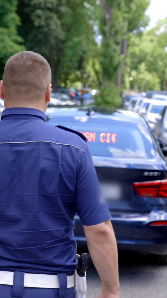 Policjant ruchu drogowego, w tle nieoznakowany radiowóz.