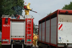 osoba w żółtym kombinezonie dezynfekuje wóz do transportu zwierząt stojąc na dachu wozu strażackiego