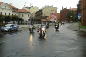 w zakręt wchodzi parada motocyklistów, a obok stoi radiowóz policyjny