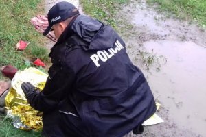 policjant pochyla się nad  mężczyzną owiniętym w folię NRC