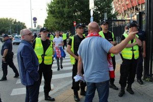 Kibic wskazuje coś policjantom, a ci uważnie słuchają