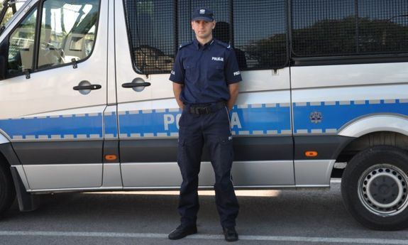 policjant stoi przed wozem policyjnym
