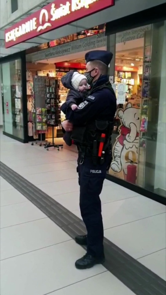 Policjant w maseczce na twarzy trzyma na rękach niemowlę.