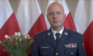 Komendant Główny Policji gen. insp. Jarosław Szymczyk na tle biało-czerwonych flag