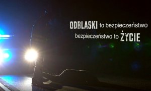 Noc, w świetle reflektorów, policjant stoi przy potrąconym człowieku. Obok napis: ODBLASKI to bezpieczeństwo, bezpieczeństwo to ŻYCIE