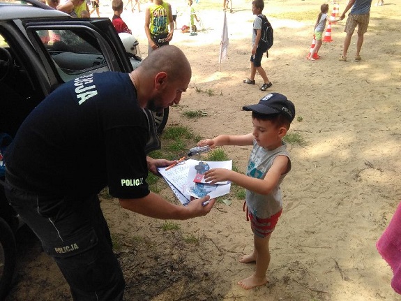 na plaży policjant stoi wspólnie z dzieckiem