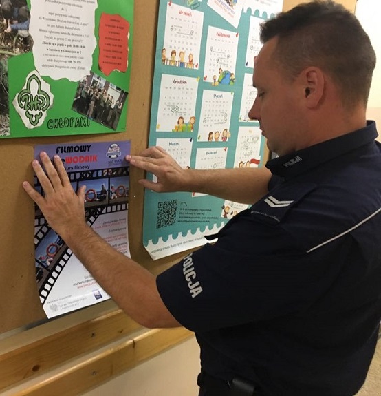 policjant wywiesza na tablicy ogłoszeń plakat konkursu pn. Filmowy przewodnik