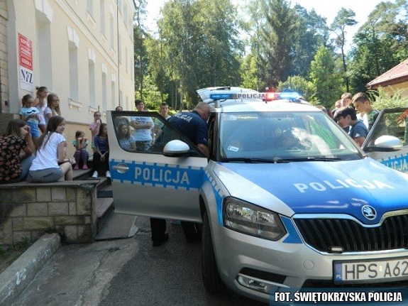 Radiowóz policyjny oraz policjanci przekazujący dzieciom zasady bezpiecznego zachowania nad wodą.