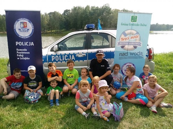 Policjant przekazuje dzieciom zasady bezpiecznego zachowania nad wodą.