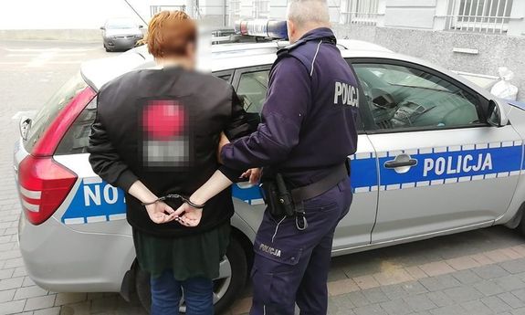 zatrzymana kobieta prowadzona przez policjanta do radiowozu