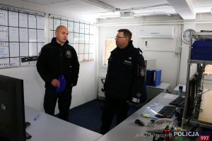 na zdjęciu sala odpraw, widać zawieszone na ścianach tablice z rozpisanymi grafikami służb, policjant wyjaśnia coś generałowi