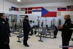 Na zdjęciu widać siłownię, policjant prezentuje gościom wyposażenie