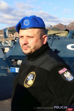 Na zdjęciu policjant w błękitnym berecie, w tle wóz bojowy