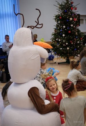 Na pierwszym planie bałwanek, tuż za nim dziewczynka, w tle choinka