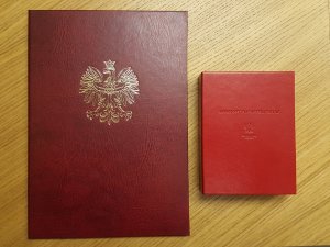 Na zdjęciu ozdobna teczka z na dokumenty z orłem na wierzchu oraz pudełko z napisem: zasłużony dla prokuratury