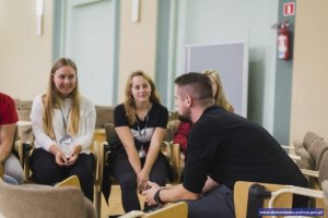 policjant rozmawia z czytelnikami, policjant na pierwszym planie, bokiem do obiektywu, na drugim planie siedzą czytelnicy przodem do obiektywu