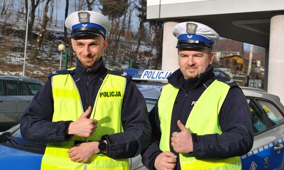 dwaj policjanci stoją przed radiowozem