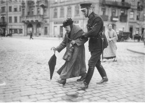 policjant przeprowadzający starszą kobietę przez ulicę