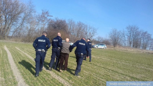 trzej policjanci razem z odnalezionym mężczyzną idę przez pole