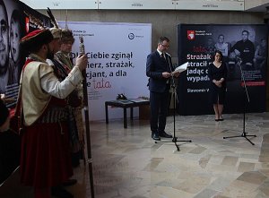 uroczyste otwarcie wystawy „Dla Ciebie zginął żołnierz, strażak, policjant, a dla mnie tata”. Po lewej mężczyźni w strojach historycznych, na środku przed mikrofonem prowadzący, z tyłu stoi kobieta